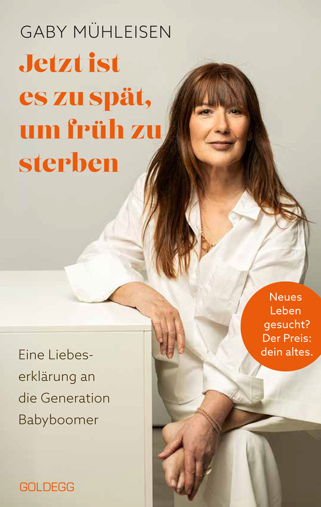 Buchcover von „Jetzt ist es zu spät, um früh zu sterben – Eine Liebeserklärung an die Generation Babyboomer“ von Gaby Mühleisen. Die Autorin sitzt in weißer Kleidung vor einem hellen Hintergrund; Titel und Gestaltungselemente sind in Orange gehalten.